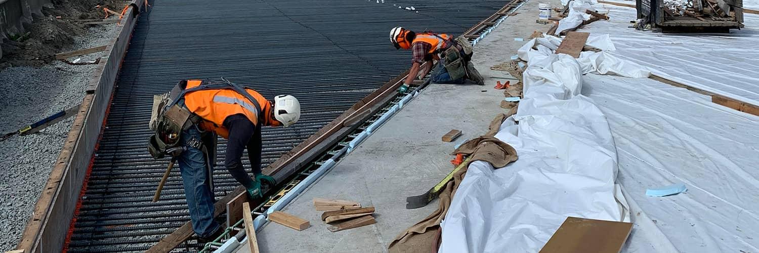 Two construction workers in hard hats laying rebar