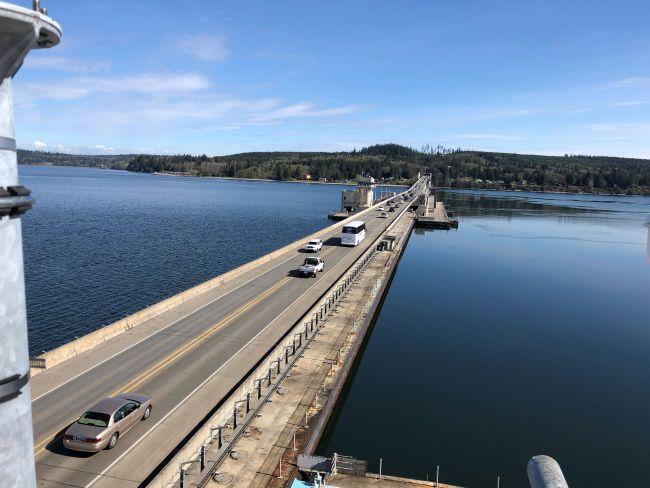 Bridge over a calm body of water with vehicles traveling under a clear blue sky.