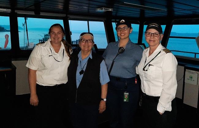 Four people posing for a photo in the wheelhouse of a ferry