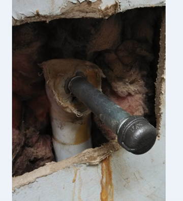 close-up picture of a hole in a wall for a plumbing repair. The galvanized pipe is capped prior to repair.