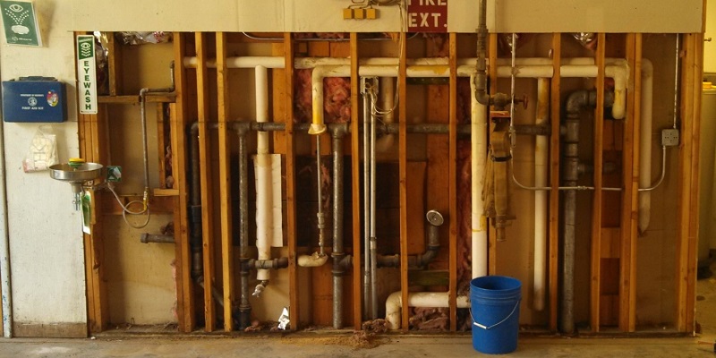 wide-angle picture of 6-foot by 10-foot wall demolition for a plumbing repair. Water supply pipes, wastewater pipes, ventilation pipes, and electrical service are all exposed.