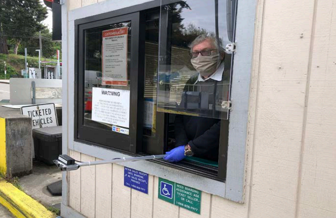 Fauntleroy toll booth ticket seller employee wears a face mask and use self-swipe credit card reader attached to a selfie stick