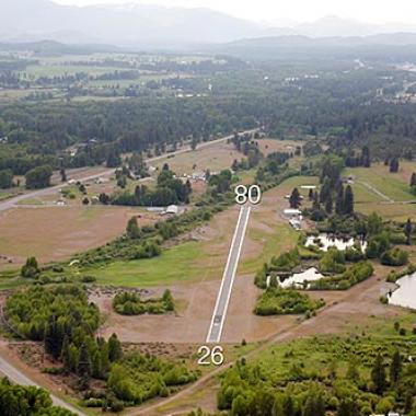 The runway at De Vere Field airport surrounded by trees and greenery. 