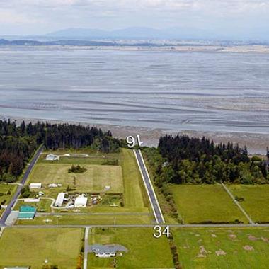 Camano Island Airport Runway located near a body of water and on flat grasslands.