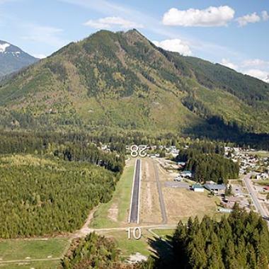 Darrington Airport runway with vast trees to the left and road to the right. 