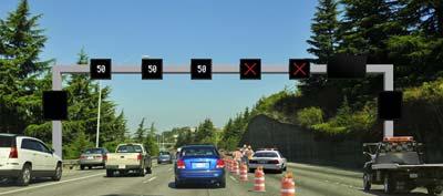 Graphic of an ATDM gantry with lanes closed.  Three left lanes show 50 MPH reduced speed limit.  Two right lanes show red X symbols for closed lanes.  Image also shows construction barrels for lane closure.