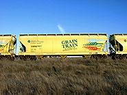 Picture of the side of a yellow grain train car moving along a field with blue skies 