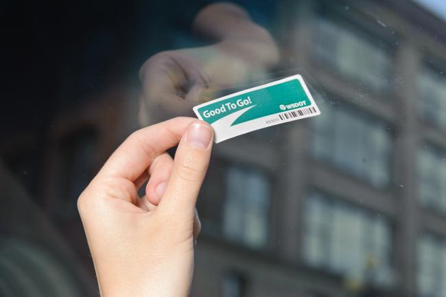 A photo showing a Good To Go sticker pass being installed on to a vehicle windshield. 