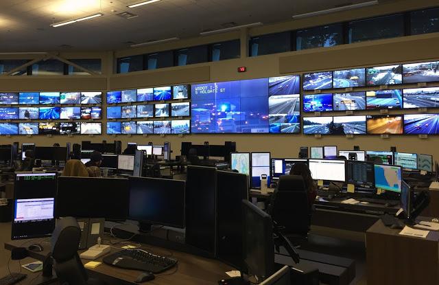 Image of WSDOT Northwest Region Traffic Management Center with workstations in foreground and monitors on far wall.
