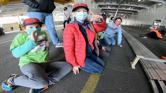 Several children on the empty car deck of a ferry near a track for a pinewood derby