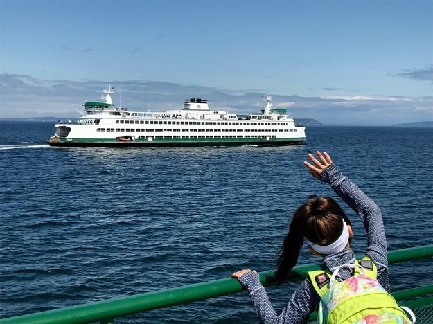 Child on the outdoor deck of a ferry waving her arm while looking at another ferry