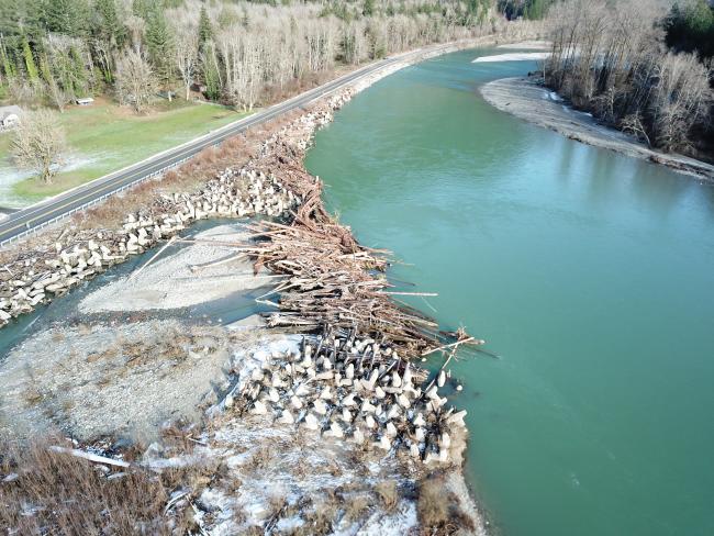 The Skagit River has migrated towards SR 20 near milepost 101, causing erosion and the need for frequent bank protection projects. Large rock protects the upstream (upper part of photo) portion of the embankment. The downstream embankment (lower part of photo) is protected by the Skagit dolotimber project – a successful, fish-friendly bank protection project installed in 2015, consisting of large concrete jacks and large wood. Photo credit: Natural Systems Design, December 2021.