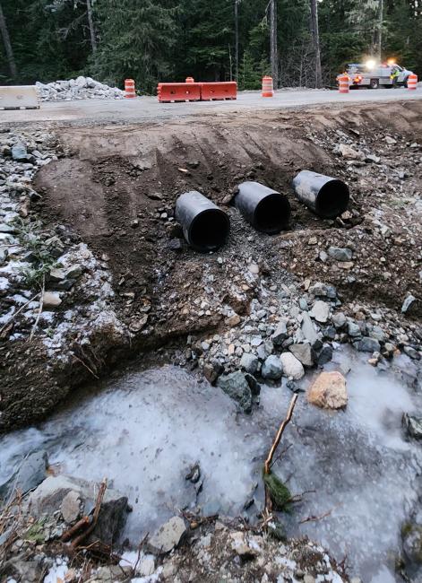Three metal, round overflow culvert are burried beneath the SR 410 roadway. In the foreground, ice is shown above the existing 24-inch culvert.