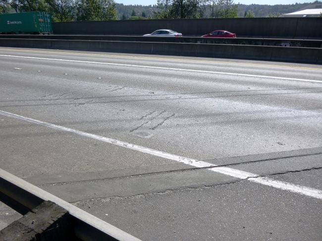 The surface of a highway bridge shows signs of wear and tear. In spots, the pavement shows rebar and the expansion joints look rough, making for a bumpy ride.