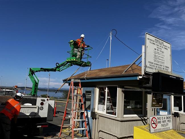 Construction worker in a cherry picker-type lift working on the roof of a tollbooth at Anacortes terminal