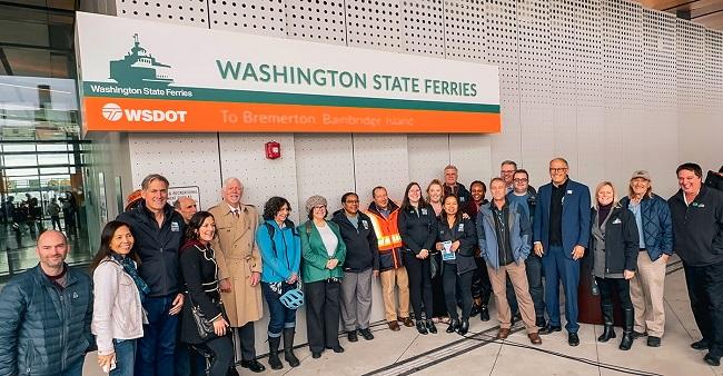 Several people posing for a photo at Colman Dock in Seattle in front of a sign on the terminal building