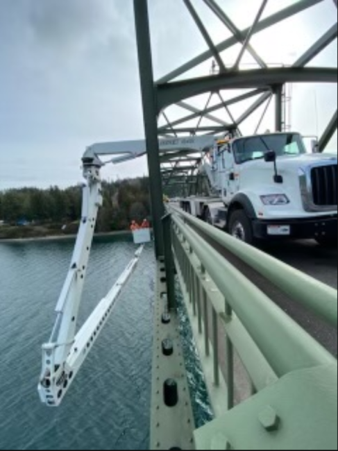 A WSDOT truck parked on the side of a green bridge with a crane overhanging the side.