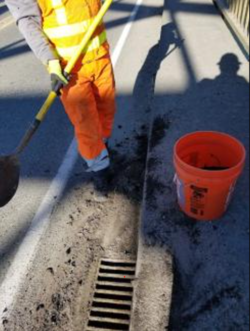 A WSDOT worker in orange safety gear shovels debris on a roadway.