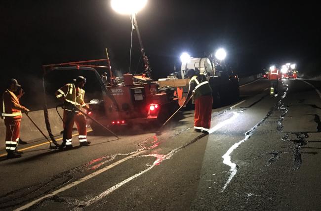 Work crews seal cracks on State Route 18 at night.