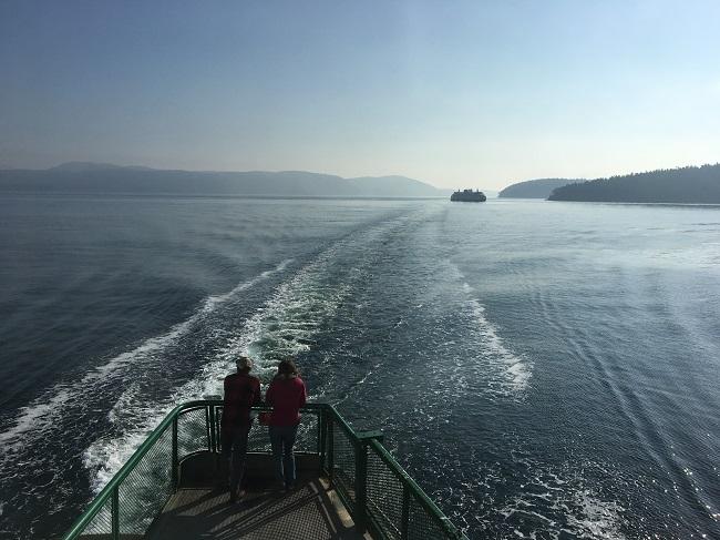 Two people on the outdoor deck of a ferry looking out at another ferry in waters around the San Juan Islands