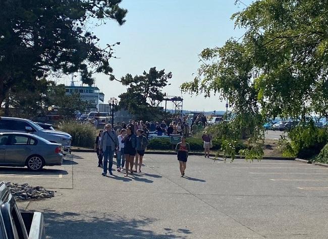 Dozens of people walking off a ferry and away from the dock into a parking lot