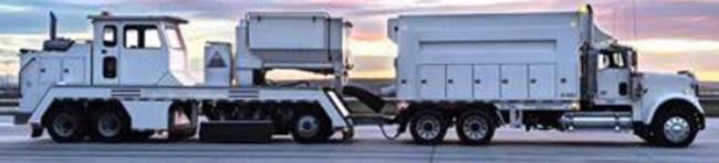 A photo showing a truck towing a machine that blasts grains into the roadway.