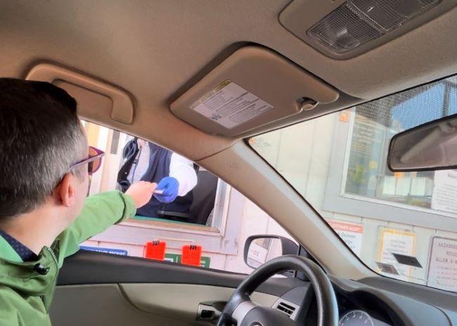 A toll booth worker wearing a blue glove hands an item to a man in a car