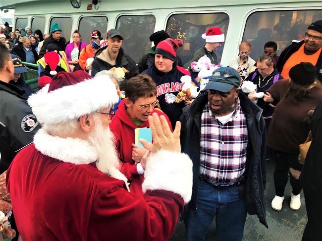 A person dressed as Santa Claus interacts with a diverse, festive crowd on a ferry