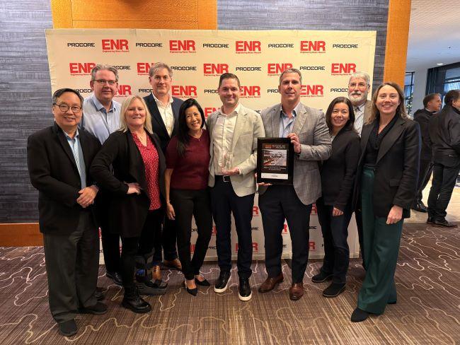 Ten people posing for a photo in front of a backdrop with the Engineering News-Record and Procore logos and one holding a crystal award and one a plaque