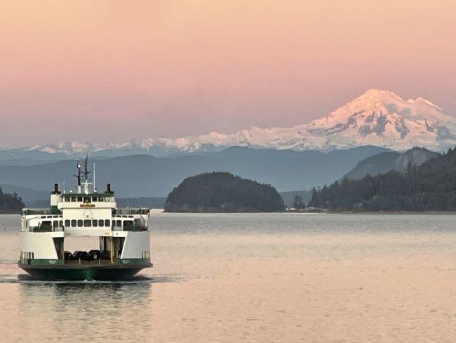 Ferry on calm water at sunset with a snow-capped mountain in the background