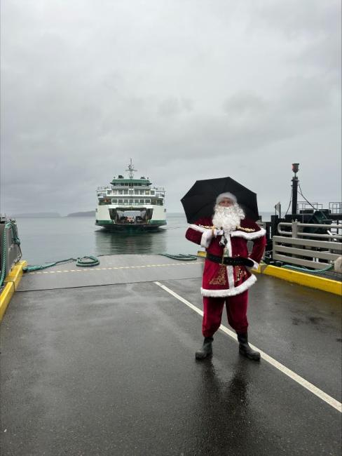 Santa Claus with an umbrella on a rainy dock, as a ferry approaches in the background