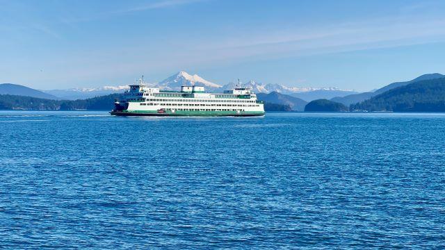 A ferry on open water with snow-capped mountains and forested shorelines in the background