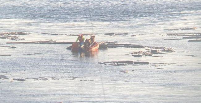 People in an orange inflatable boat on water amidst debris or logs A ferry worker assists a person in a motorized wheelchair onto a ferry