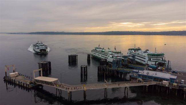 Ferry terminal with three ferries; two docked and one approaching, under a cloudy sky