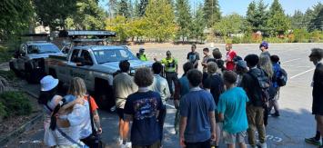 A group of young students gather around WSDOT workers and an incident response truck in a parking lot.