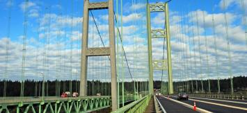 Both spans of the Tacoma Narrows Bridge with cars traveling across, road cones separating one lane.